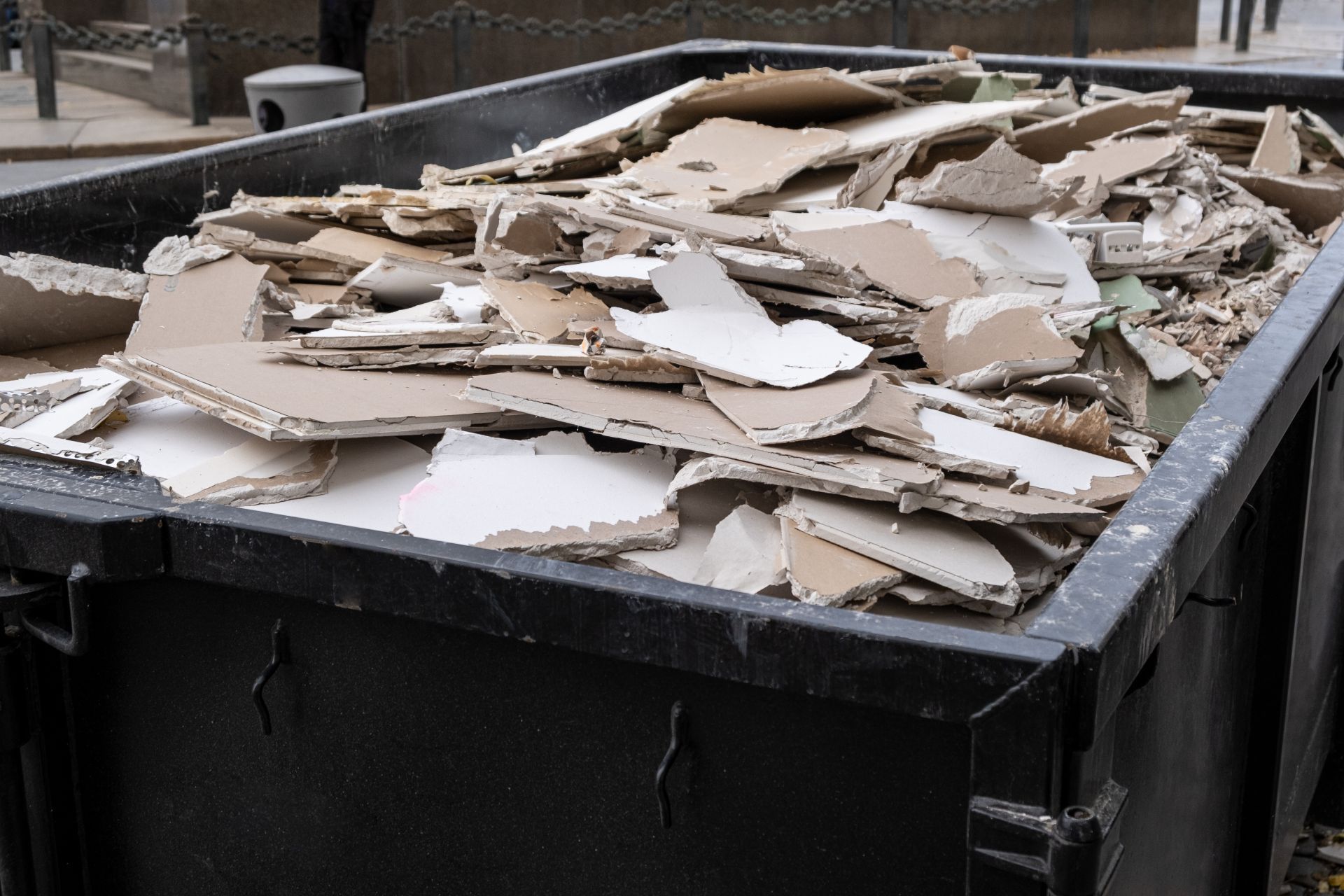 Black dumpster filled with broken pieces of white and brown drywall.