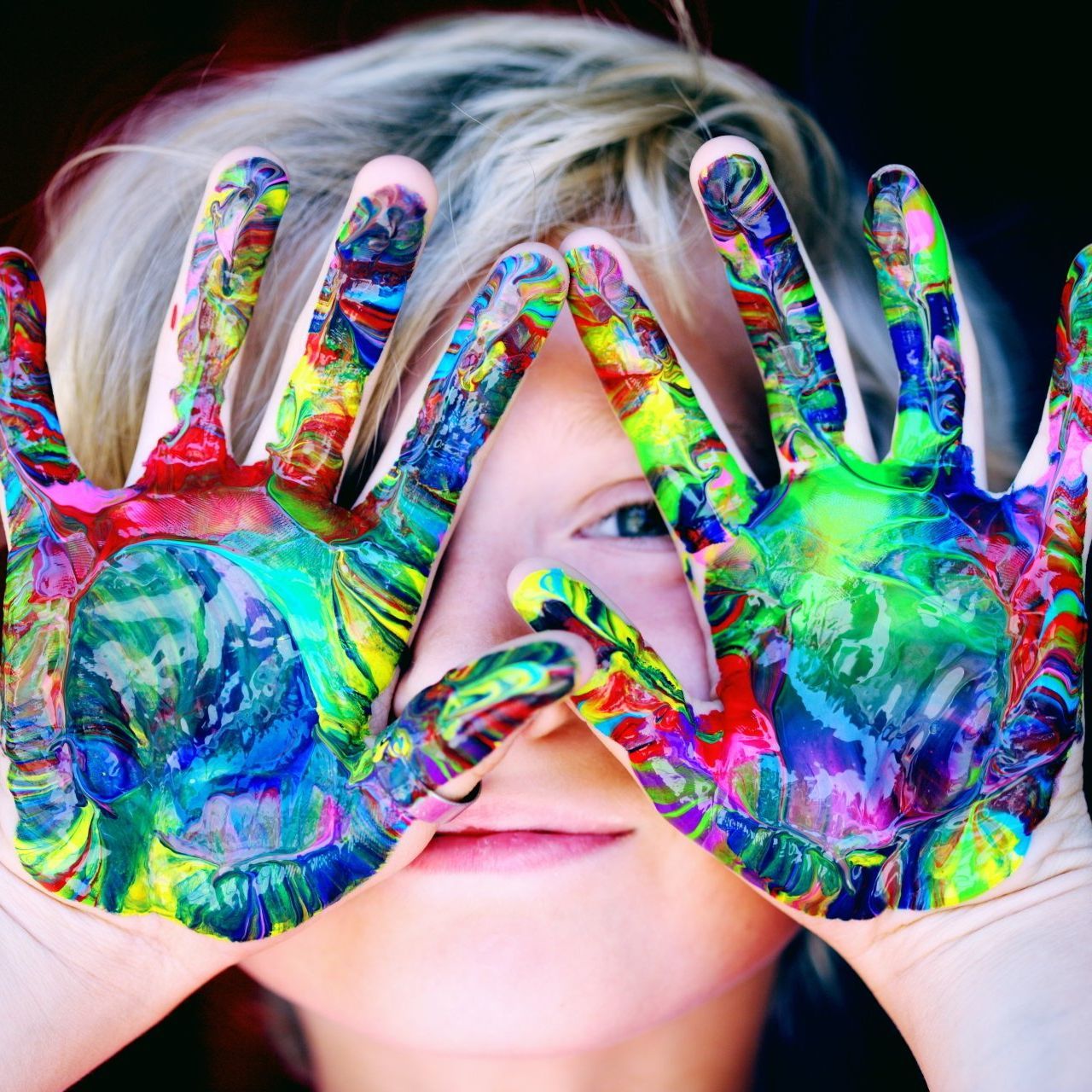 a child covering face with hands painted in different colors representing Play Therapy for children.