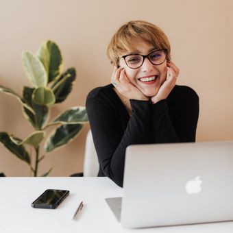 a woman wearing glasses is smiling in front of an apple laptop just about to step into an Online Counselling session