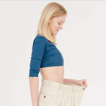 a woman is wearing a blue crop top and white pants that are over-sized before struggling with Weight Loss and Obesity