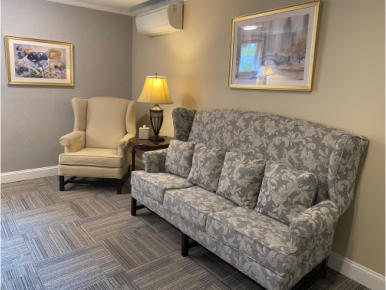 Cozy waiting area with sofa, armchair, table with lamp, art on walls, and patterned carpet.
