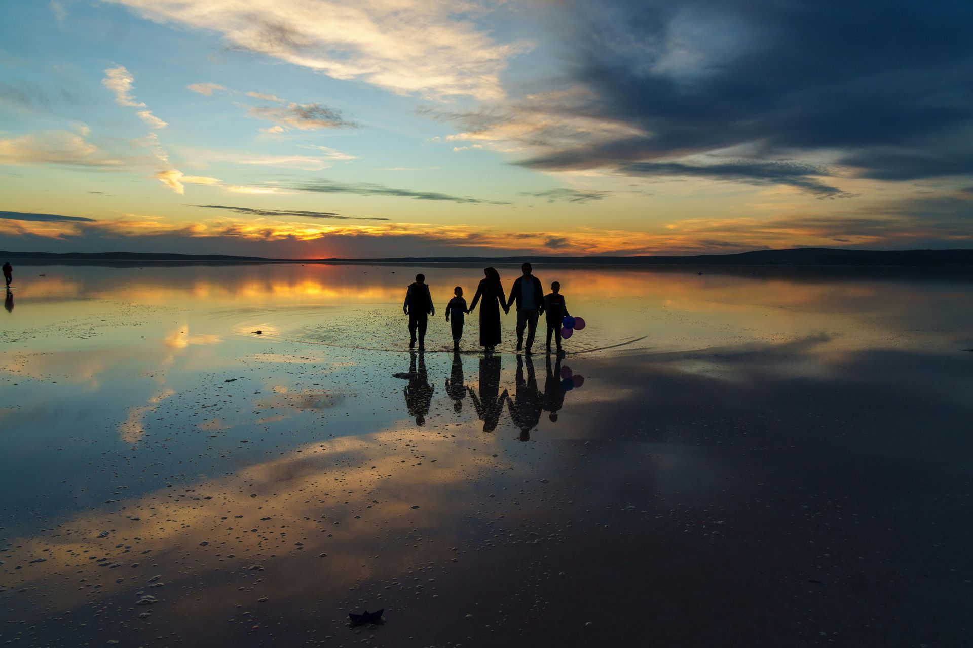 Family walking on a reflective lake at sunset; colorful sky reflects in water.