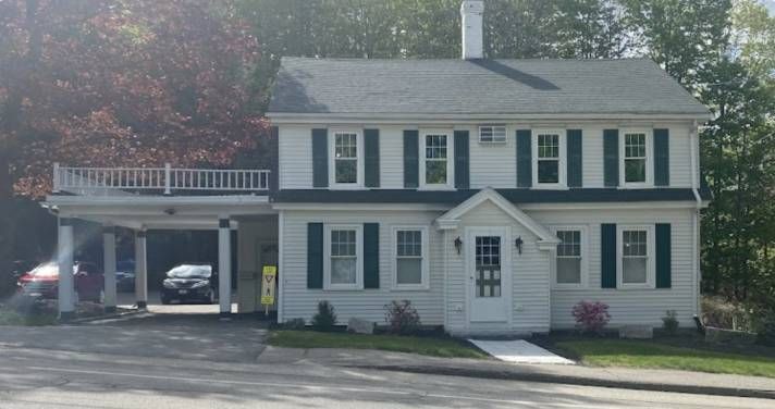 White two-story house with green shutters, attached carport with cars, and a small balcony.