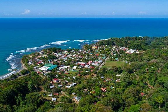 An aerial view of a small town surrounded by trees next to the ocean.