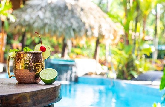 A drink is sitting on a table next to a swimming pool.