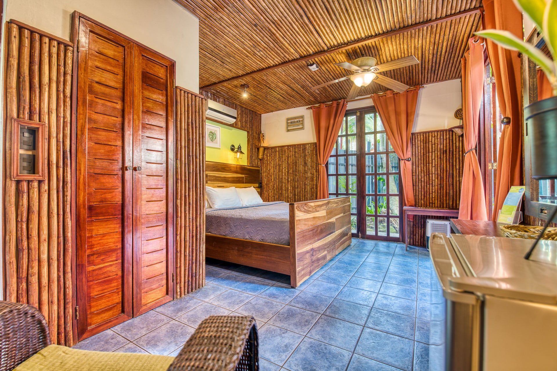 A hotel room with a bed , a chair , a refrigerator and a ceiling fan.