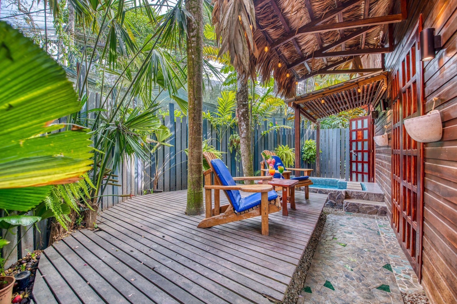 A wooden deck with chairs and a table under a thatched roof.