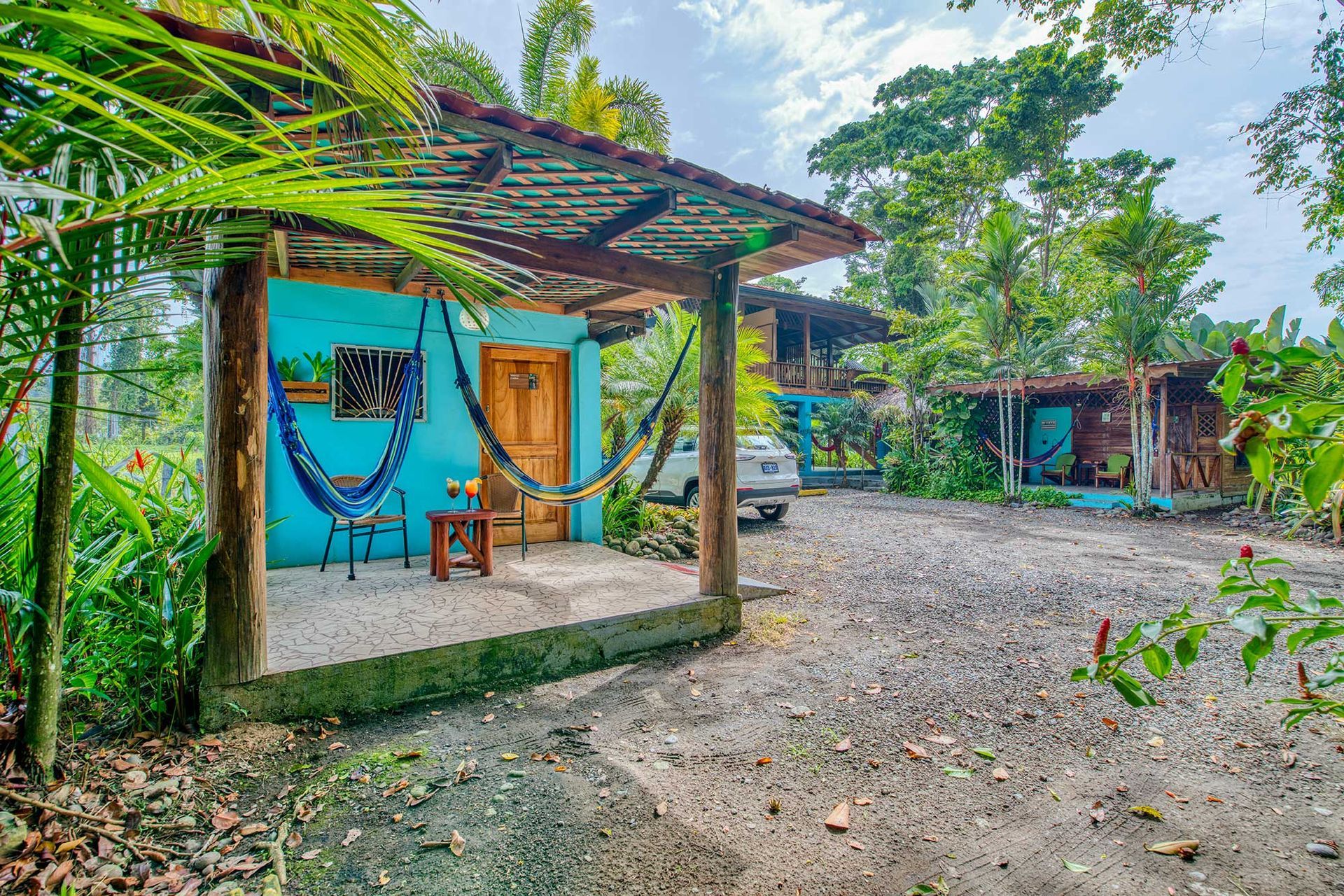 A small blue house with hammocks on the porch and a car parked in front of it.