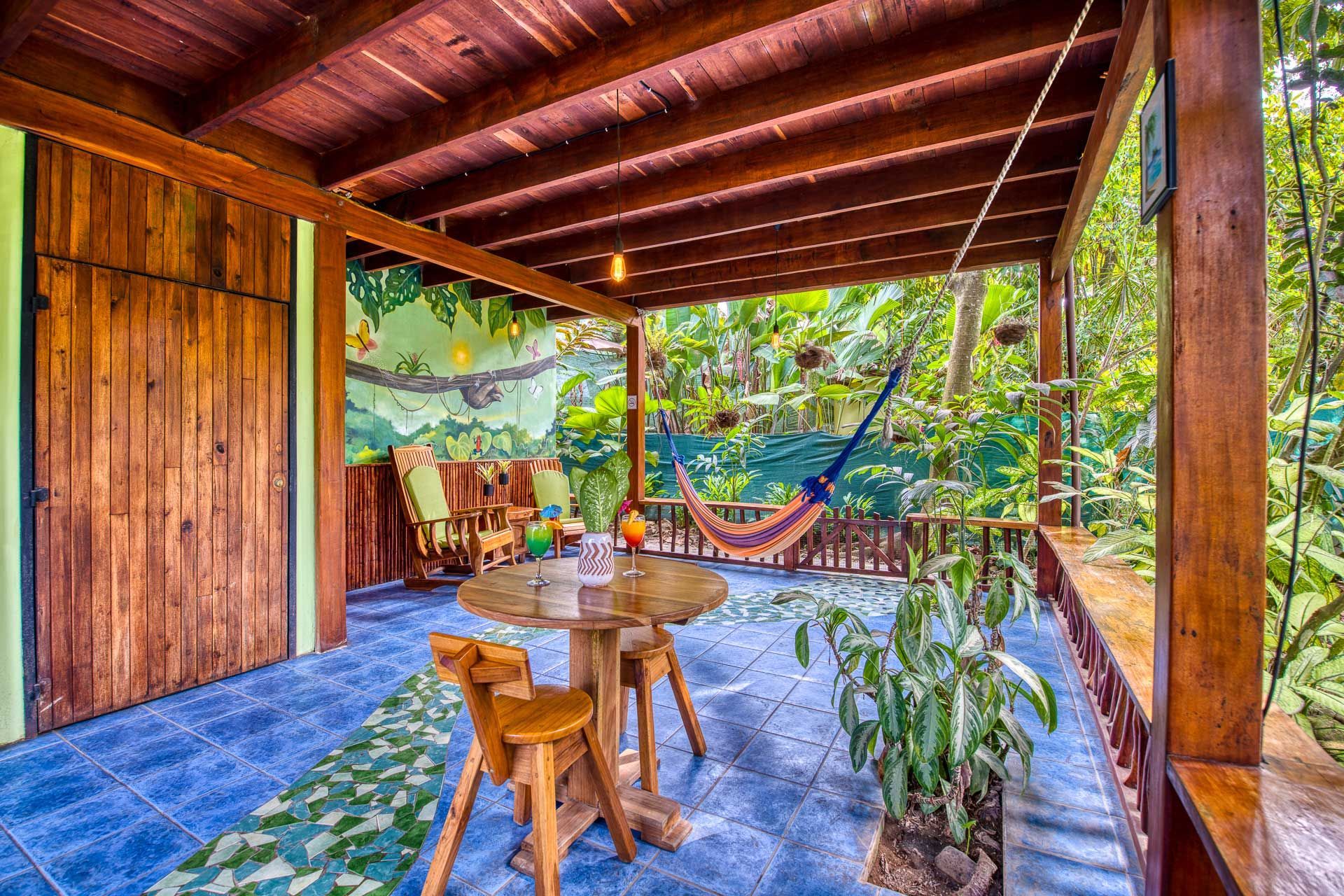 A wooden porch with a table and chairs and a hammock hanging from the ceiling.