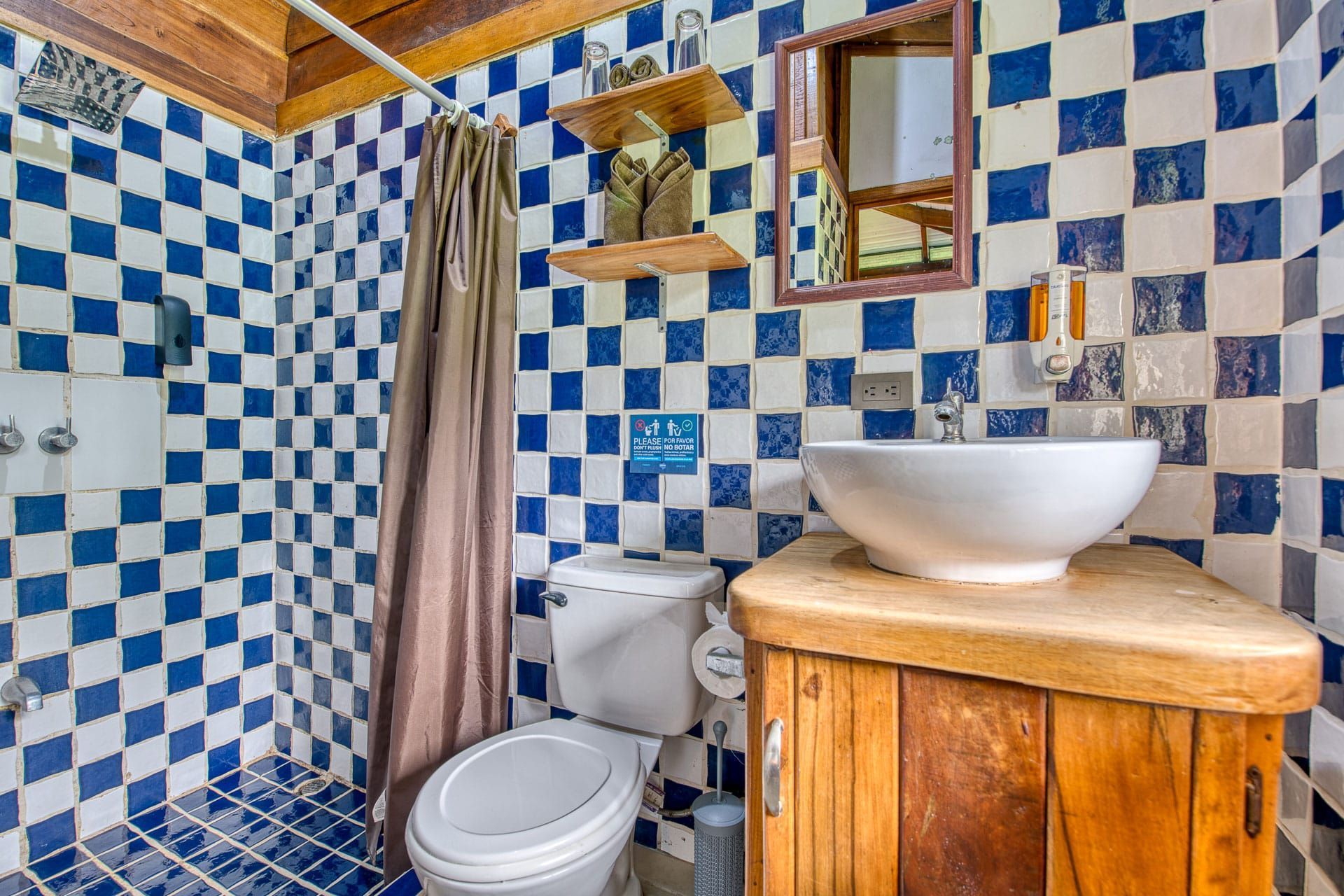 A bathroom with blue and white checkered tiles , a toilet , sink and mirror.