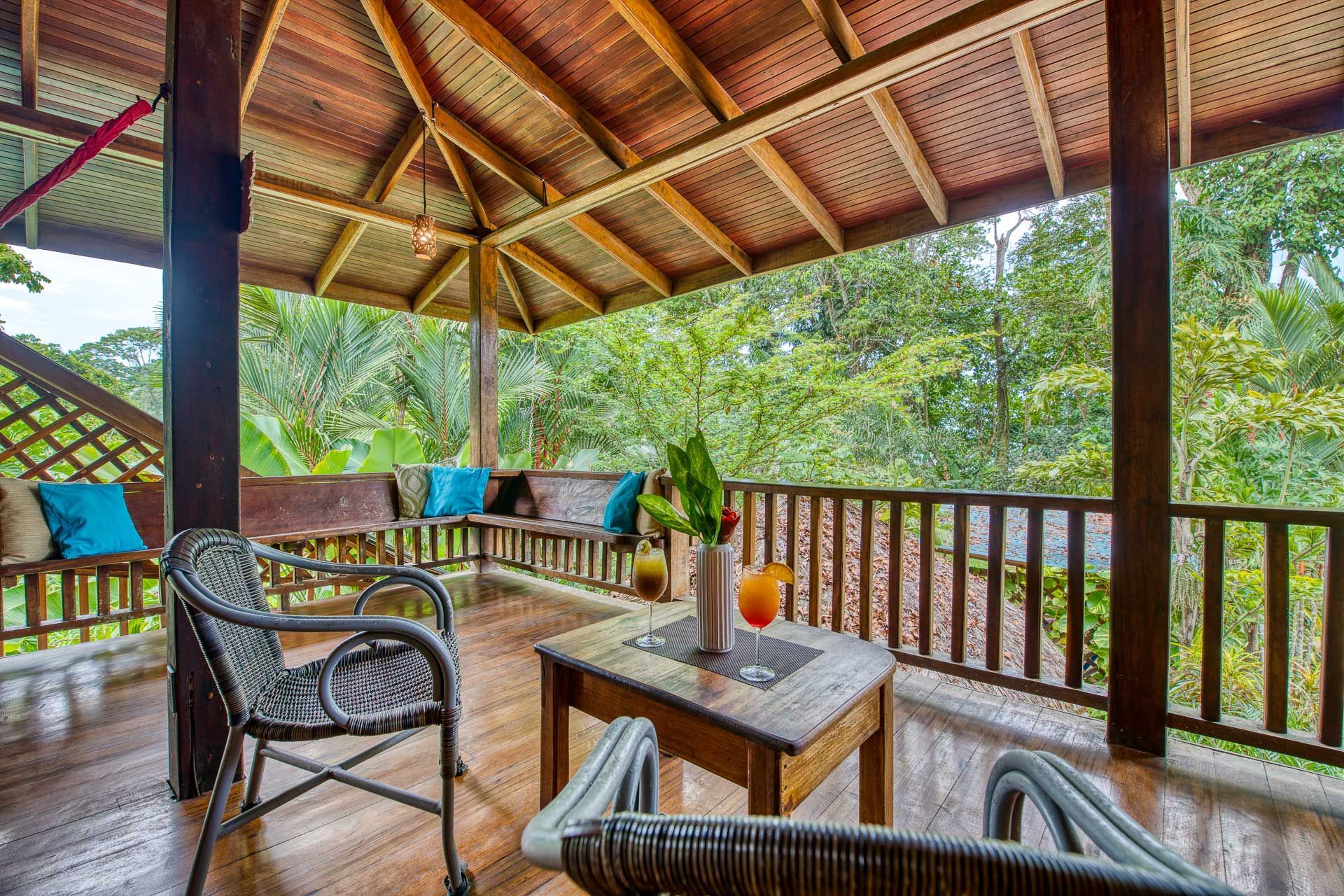A wooden porch with chairs and a table with a view of the trees.