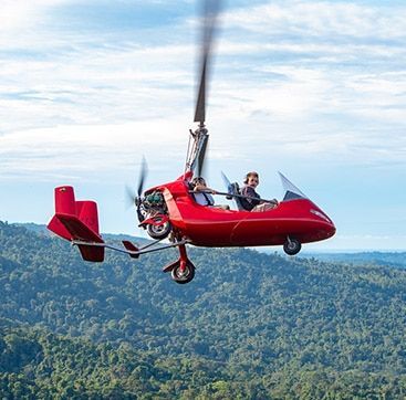 A red helicopter is flying over a forest.