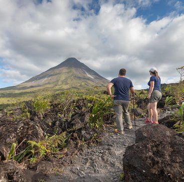 A man and a woman are standing on a rocky path looking at a mountain.
