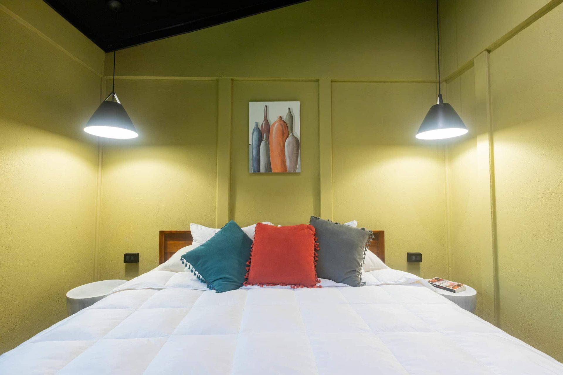 A bedroom with a bed , pillows , lamps and a painting on the wall.