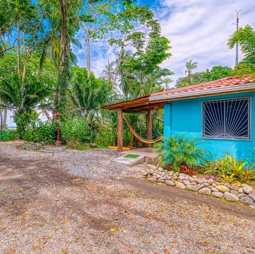A blue house with a hammock in front of it in the jungle.