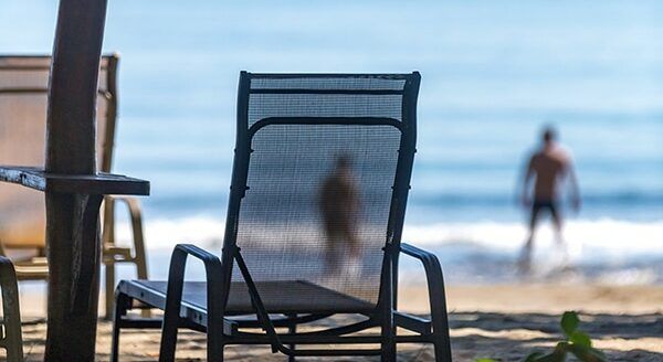 Mesh beach chairs face the ocean, where blurred figures walk along the shoreline.