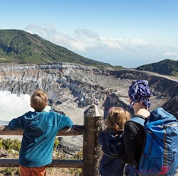 A group of people are standing on top of a mountain looking at a volcano.