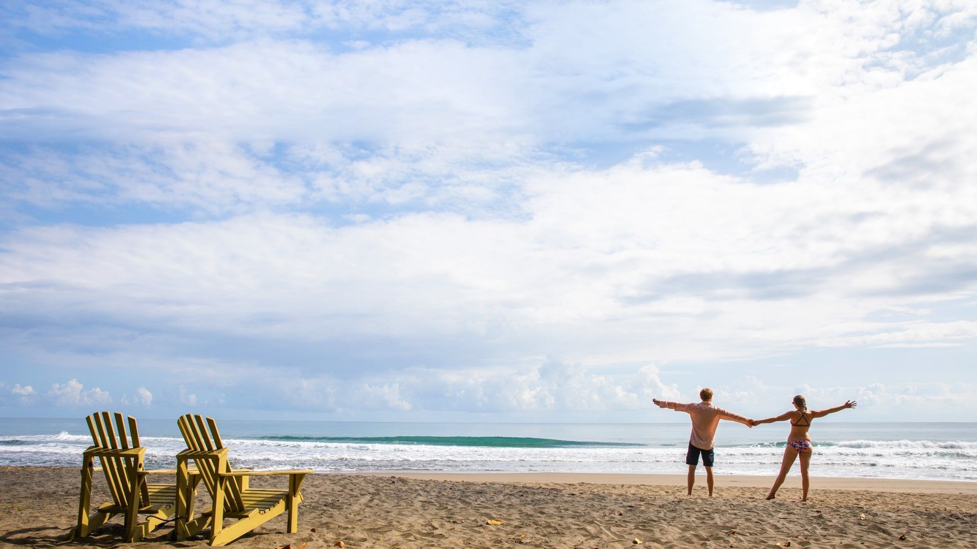 A man and a woman are standing on a beach with their arms outstretched.