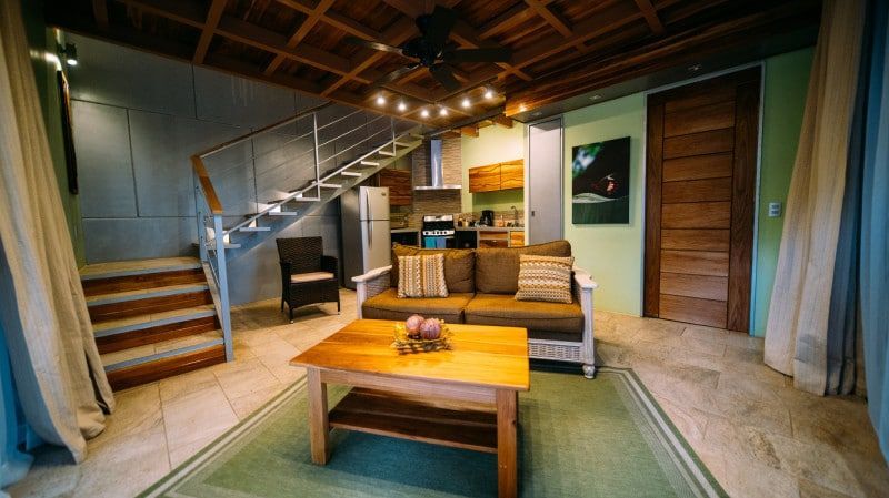 A living room with a couch , coffee table , and stairs leading to the kitchen.