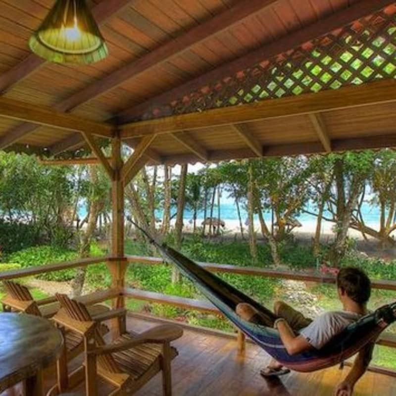 A man is laying in a hammock on a porch overlooking the ocean.
