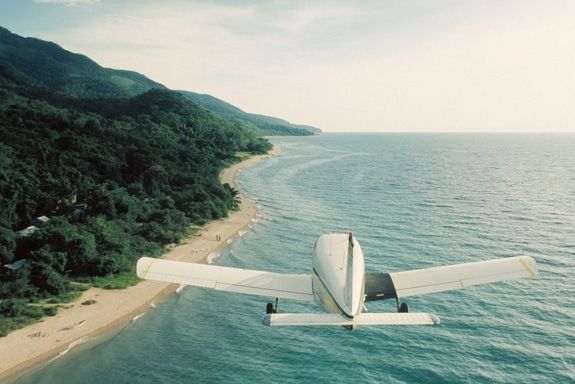 A small plane is flying over the ocean near a beach.