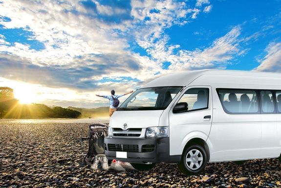 A white van is parked in the middle of a rocky field.