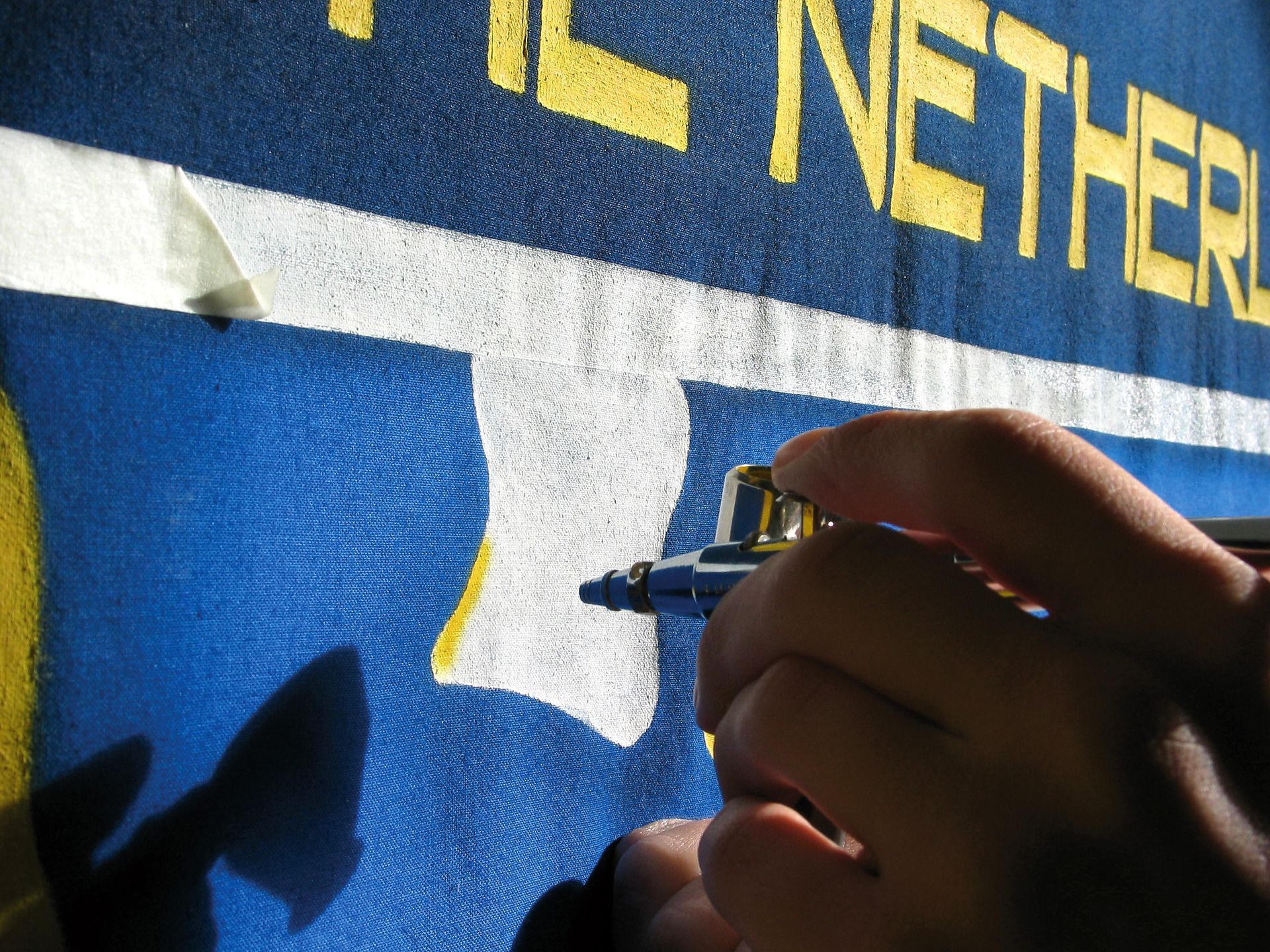 Met een airbrush worden gele letters op een blauwe ondergrond geschilderd, met het woord 