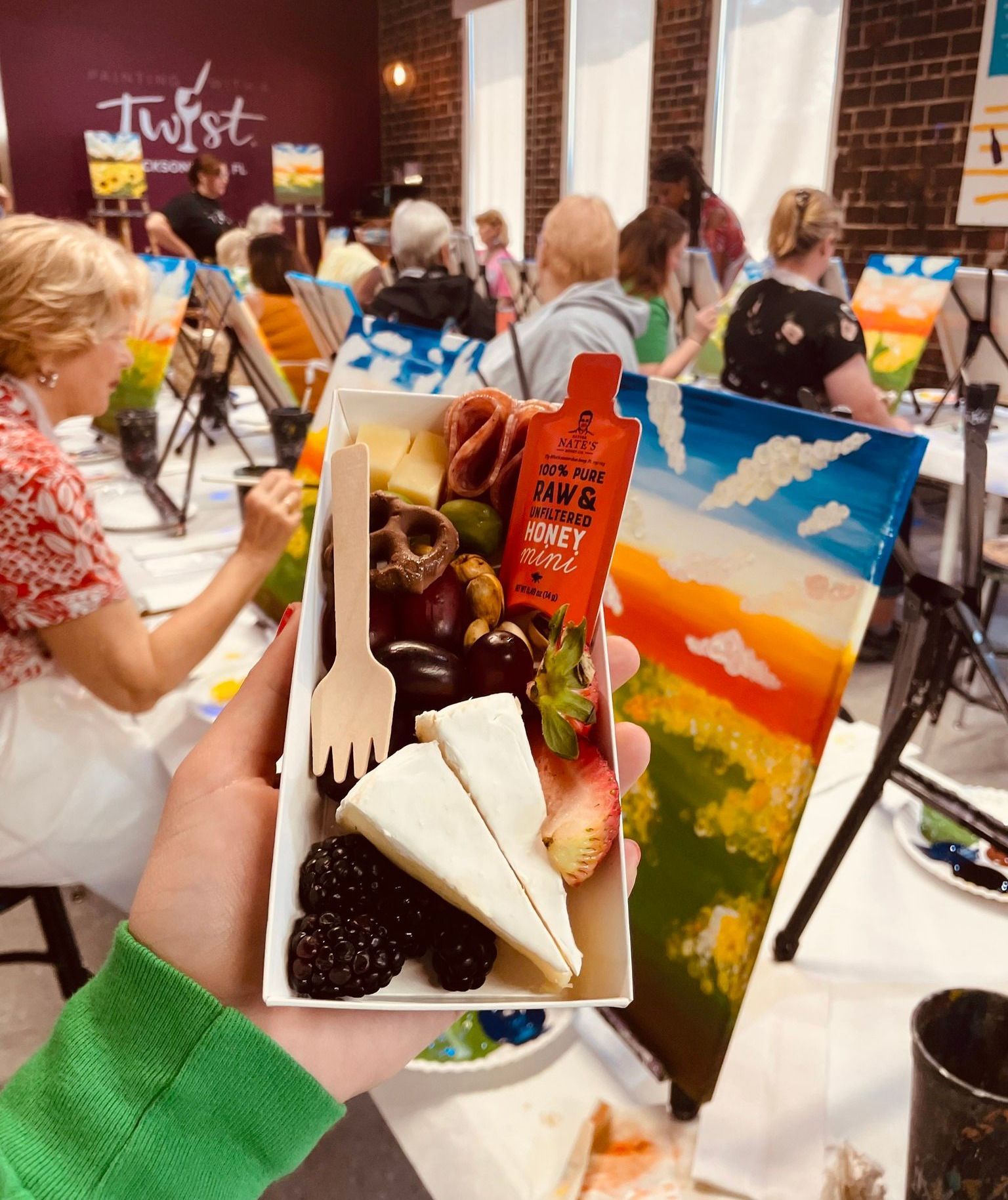 A person is holding a box of food in front of a painting.