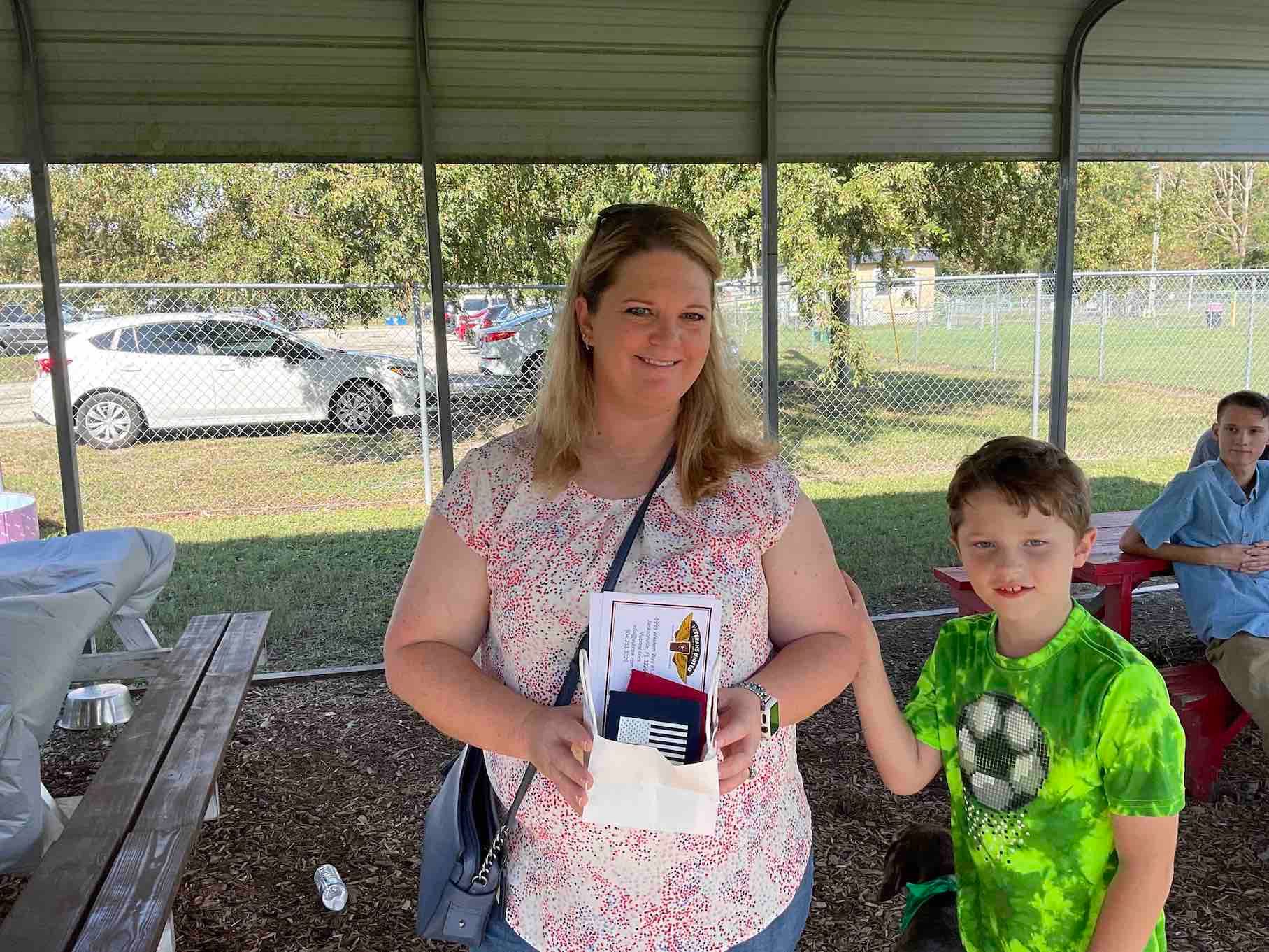 A woman is holding a box next to a boy in a green shirt.