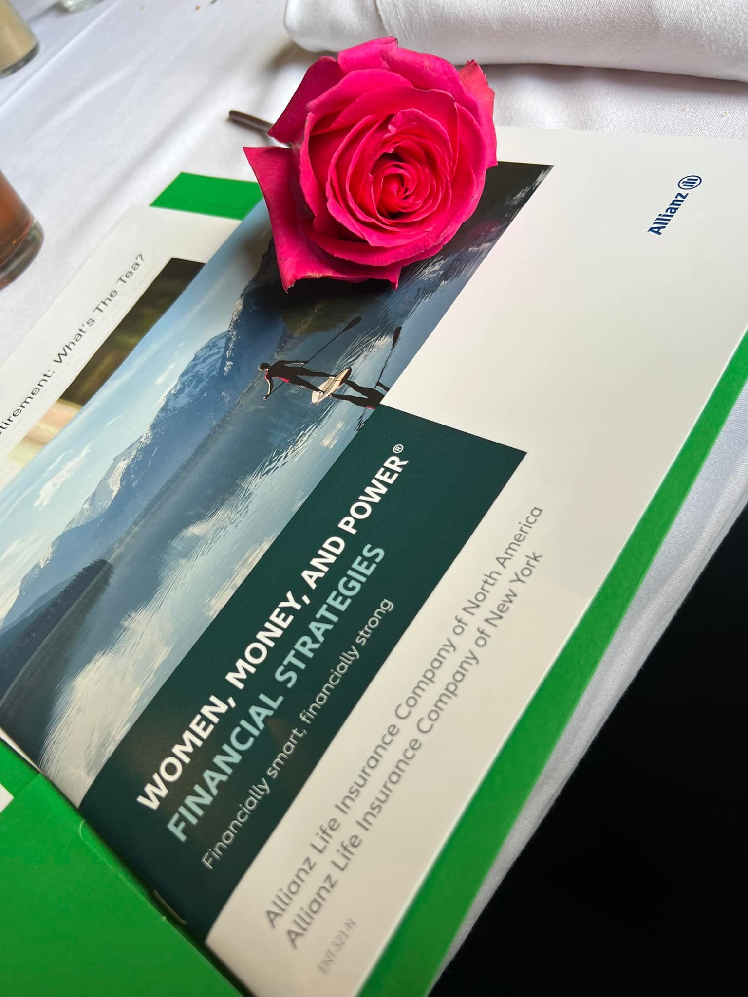 A pink rose sits on top of a book titled women money and power financial strategies