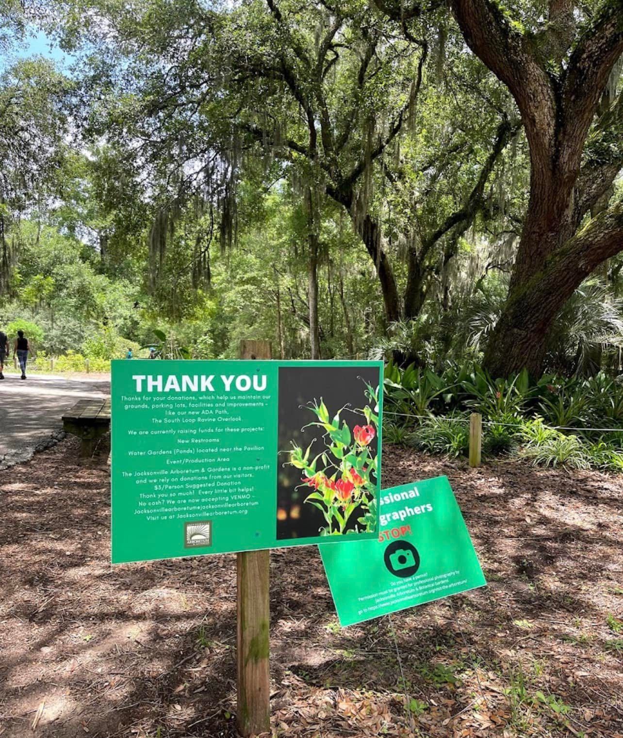 A thank you sign is sitting on a wooden post in the woods.