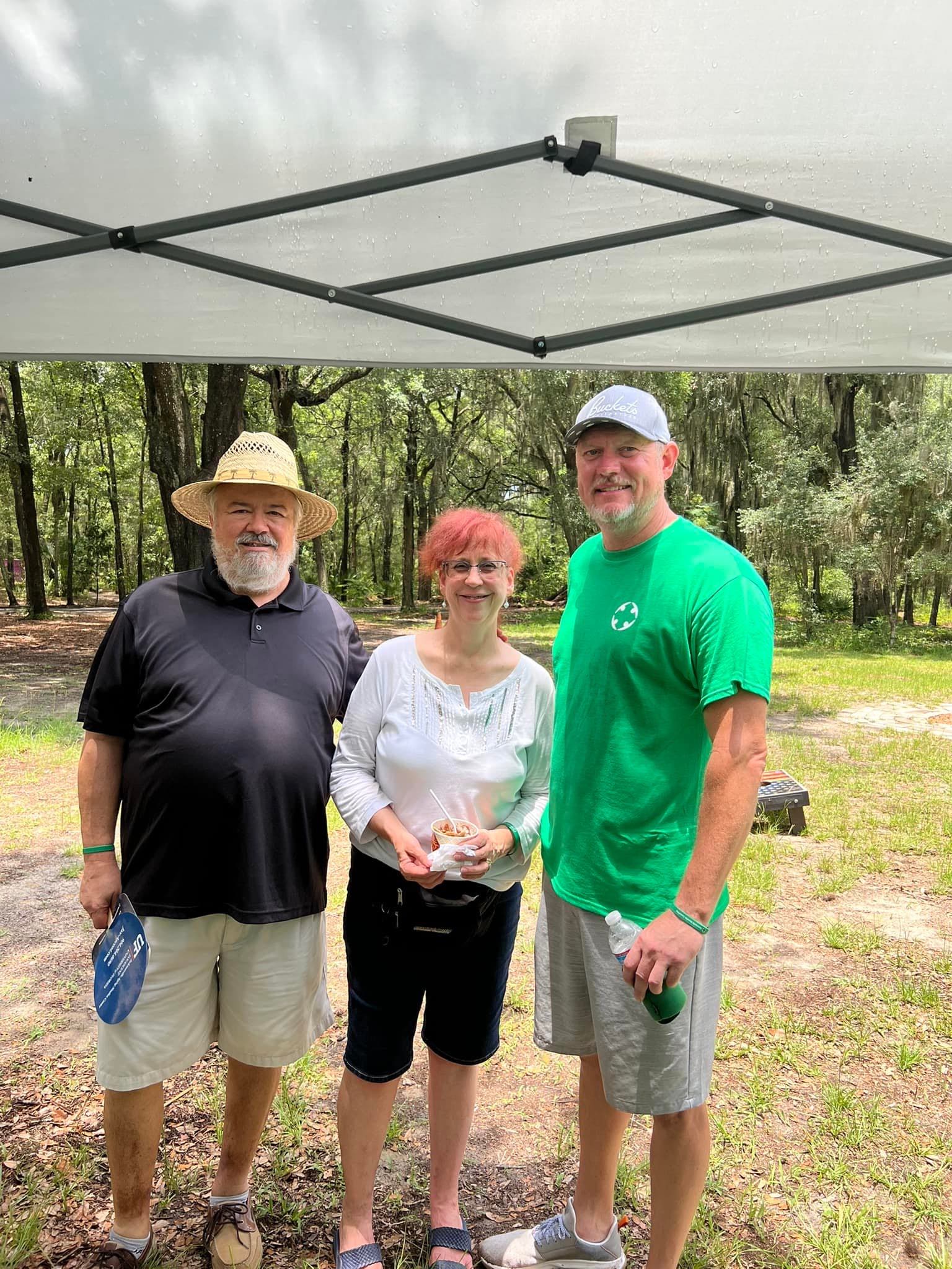 A man in a green shirt is standing next to a woman and a man in a black shirt.