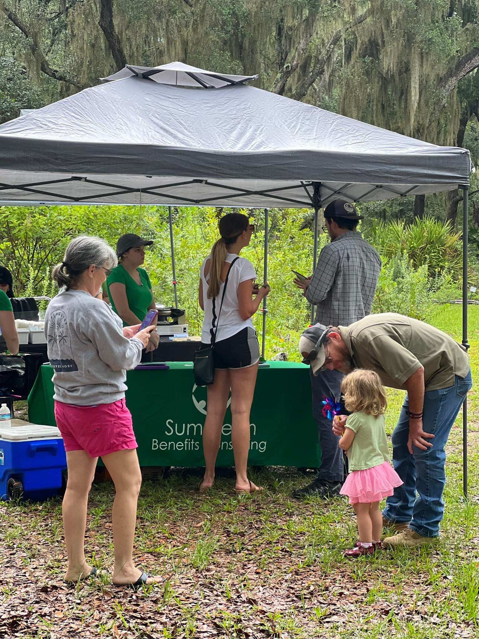 A group of people are standing under a tent in a field.