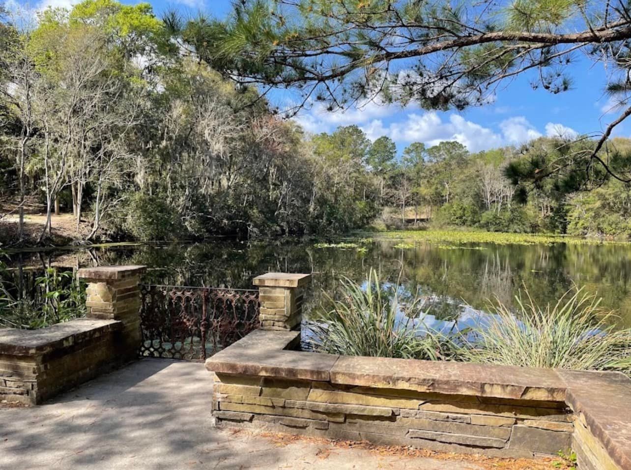 There is a stone wall surrounding a lake with trees in the background.