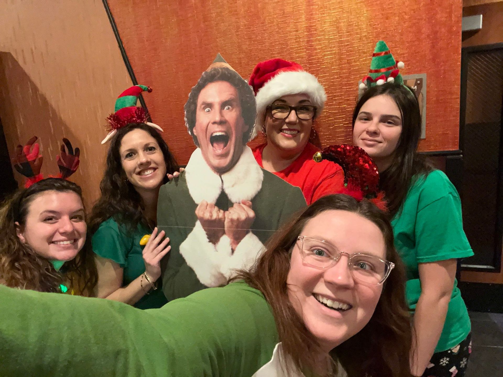 A group of women are posing for a picture with a cardboard cutout of eddie the elf.