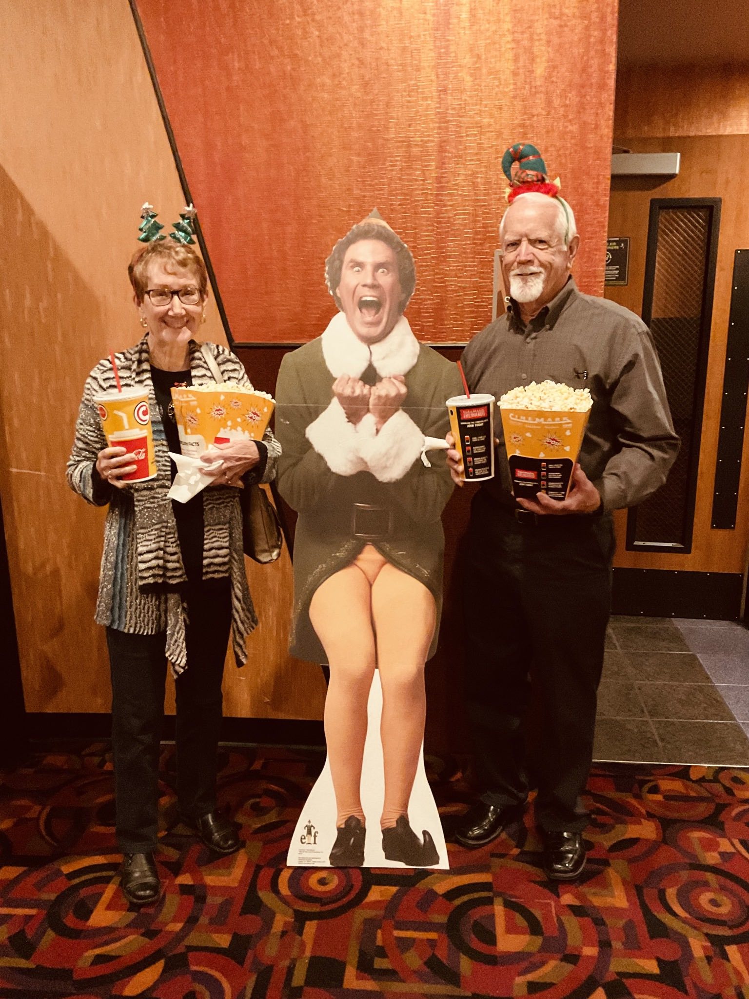A couple of people standing next to a cardboard cutout of elf