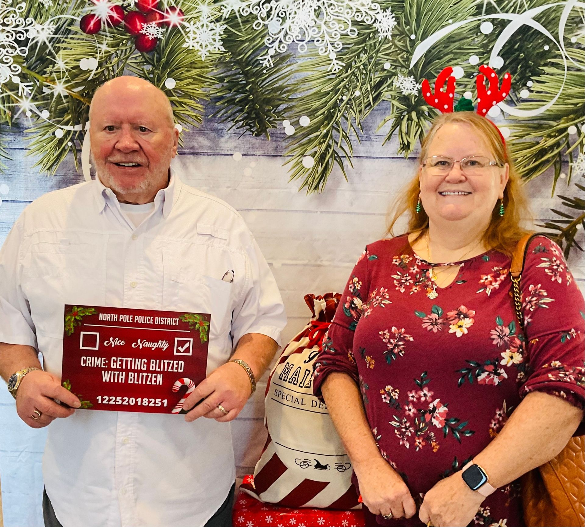 A man and a woman are posing for a picture in front of a christmas background.