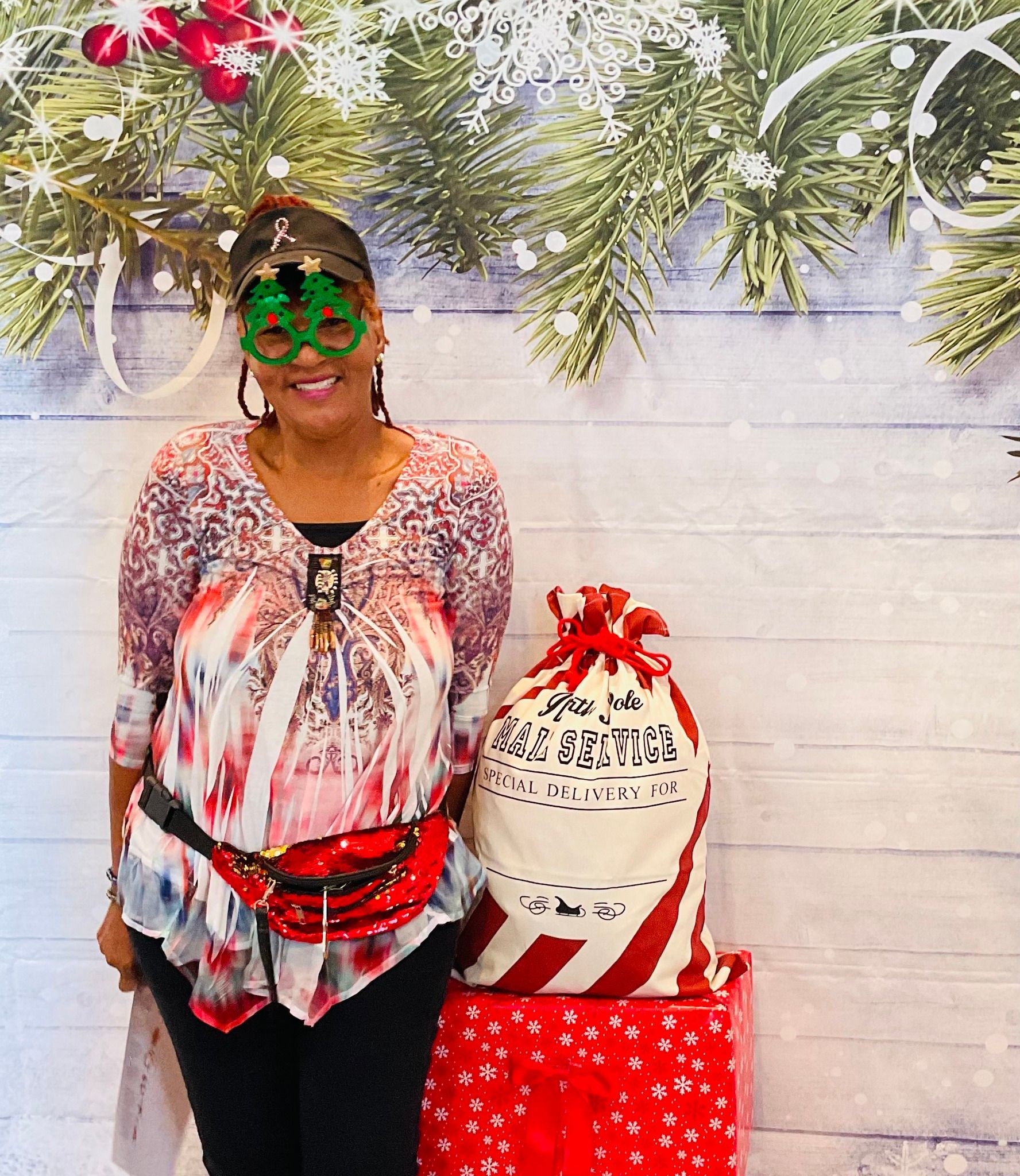 A woman wearing green glasses is standing in front of a christmas background.