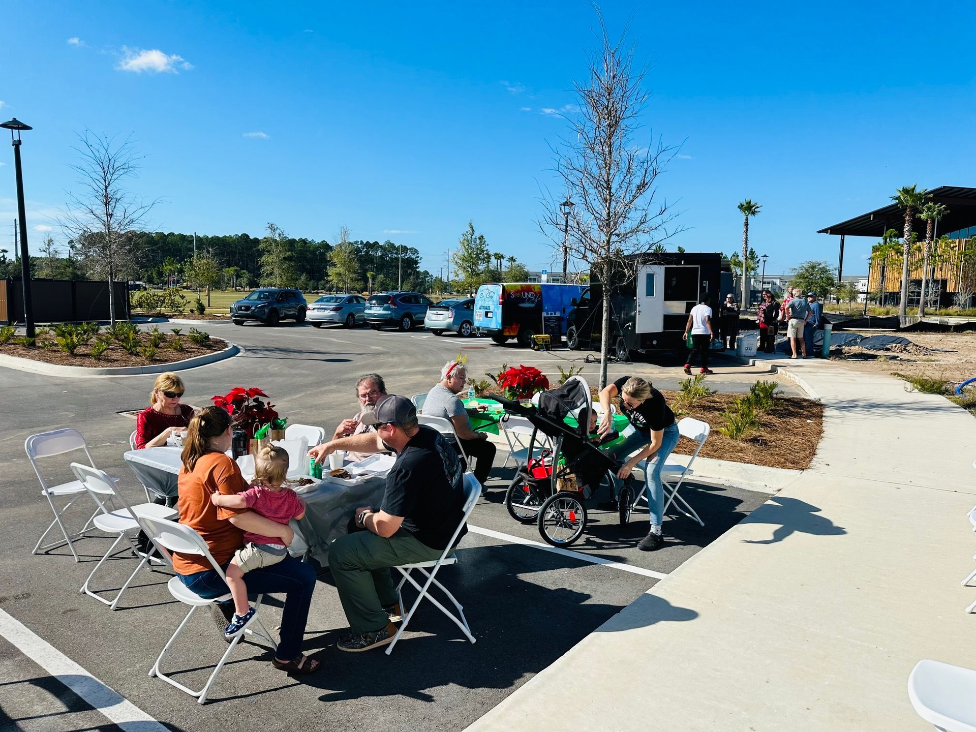 A group of people are sitting at tables in a parking lot.