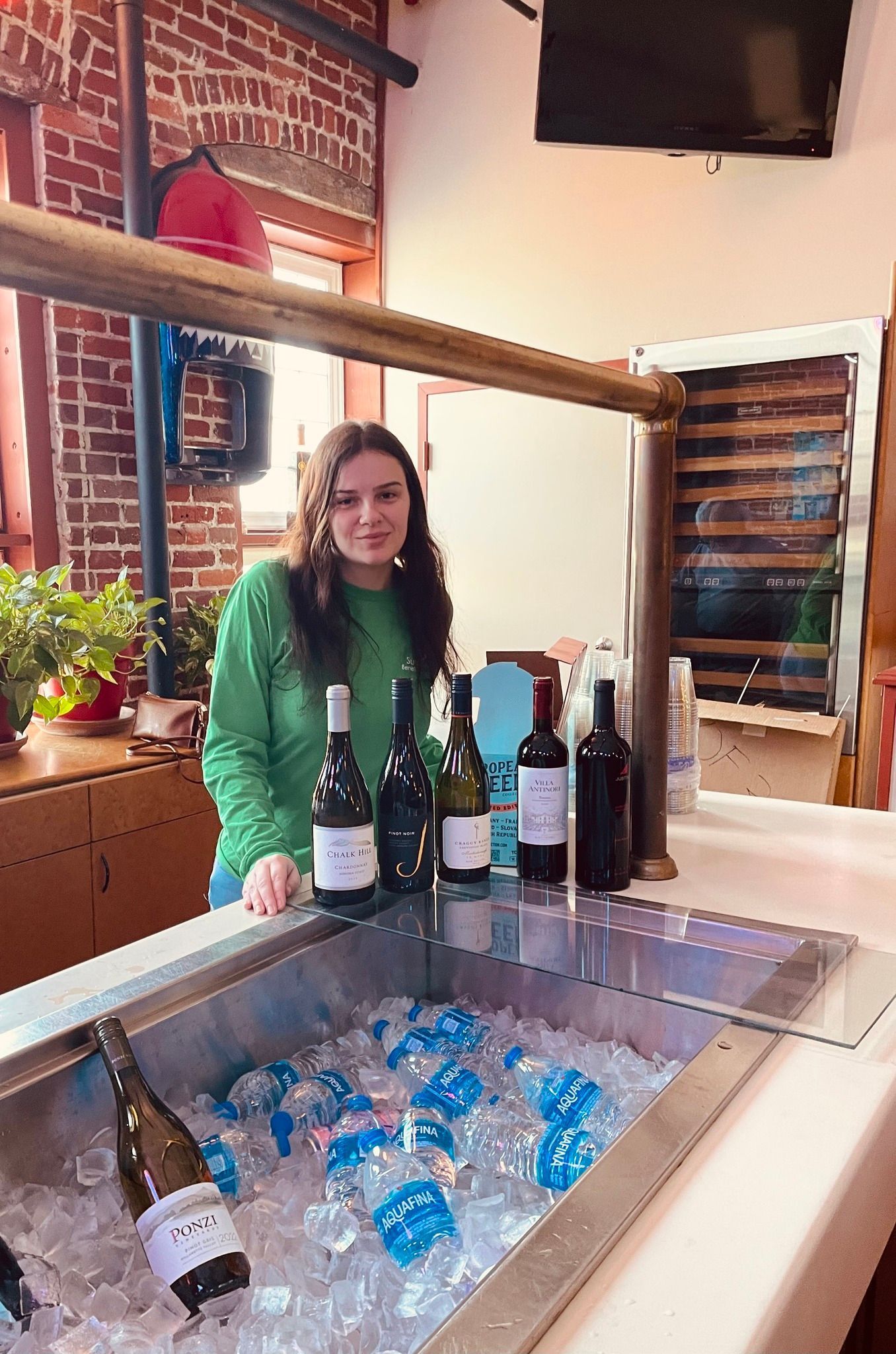 A woman is standing in front of a sink filled with ice and wine bottles.