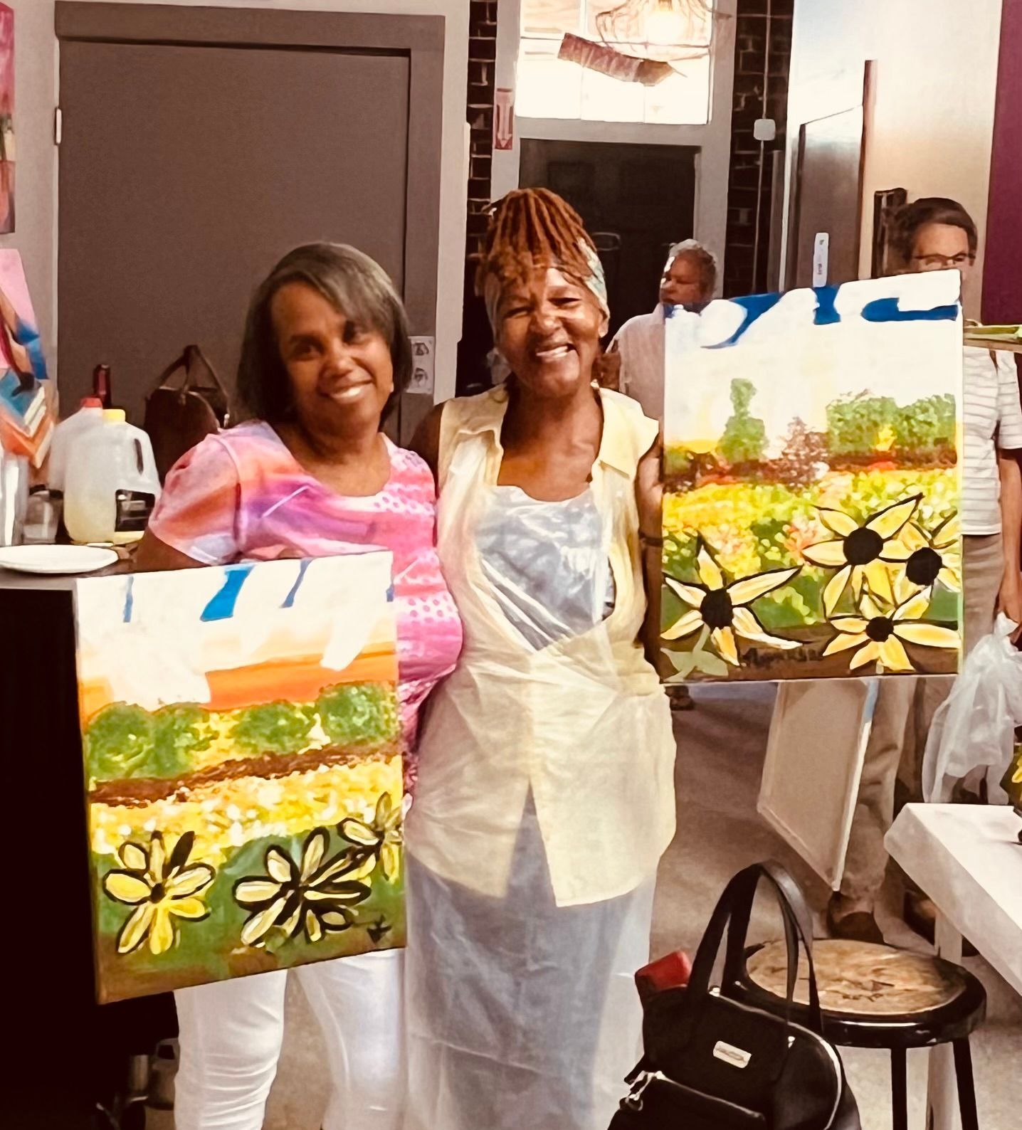 Two women standing next to each other holding paintings of flowers