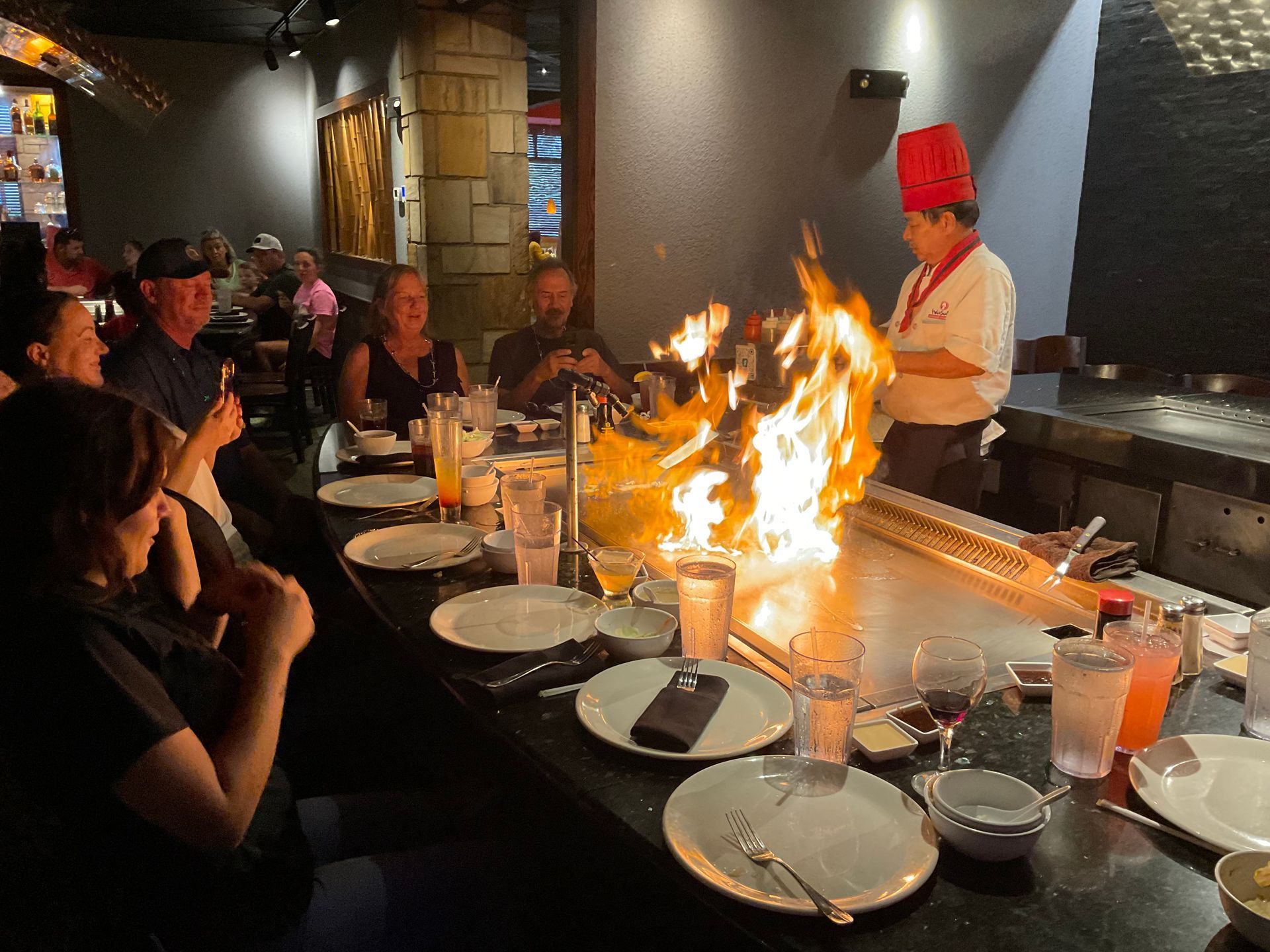 A group of people are sitting at a table in a restaurant watching a chef cook