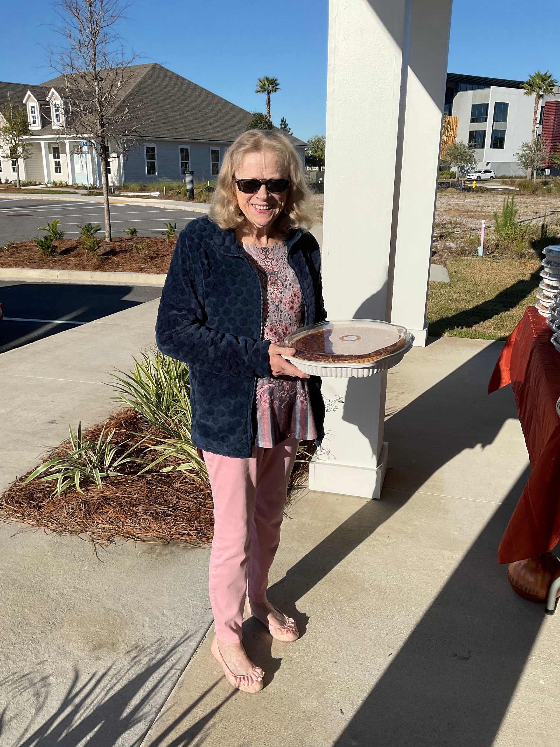 A woman is standing on a sidewalk holding a tray of food.