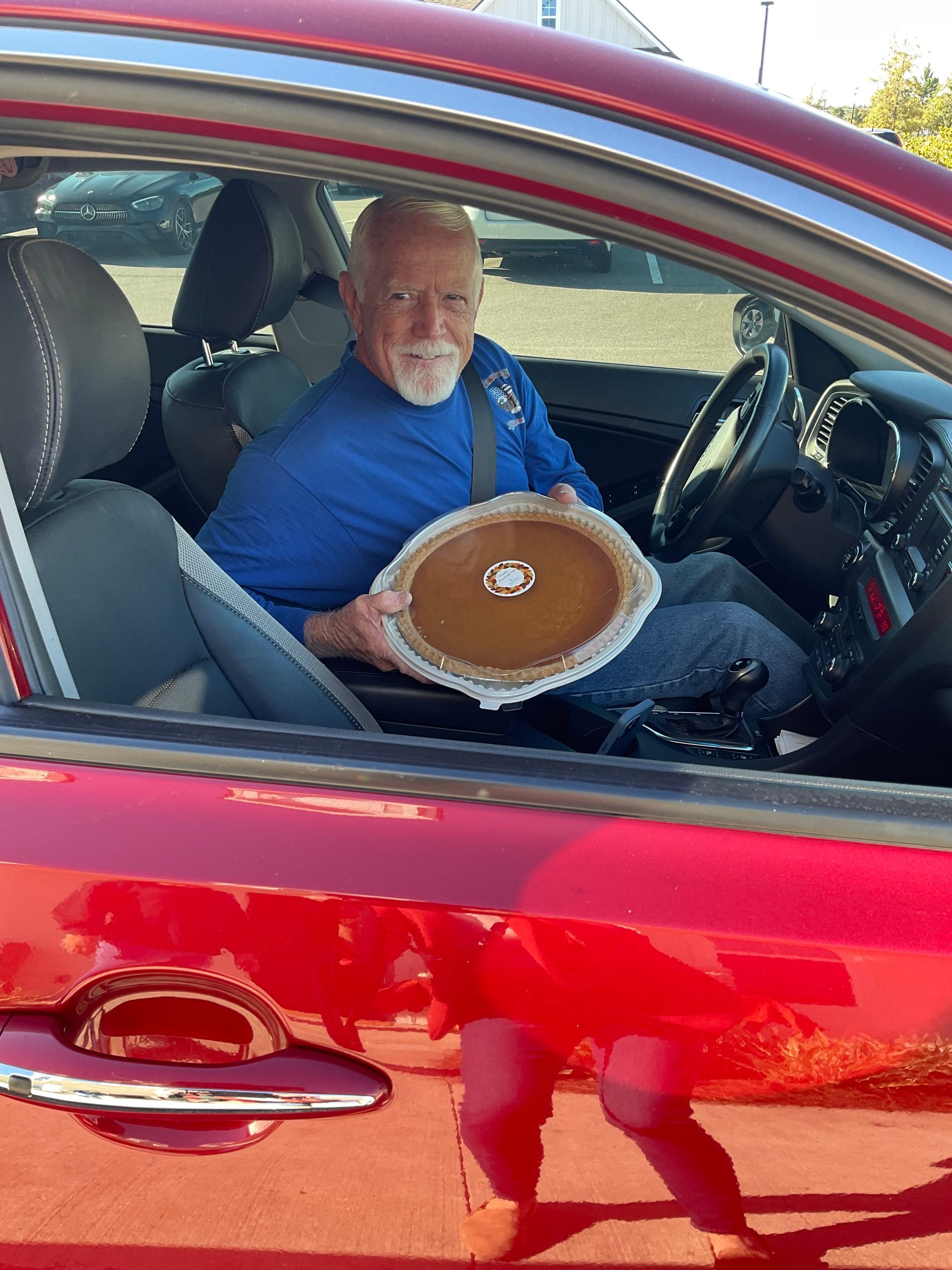 A man is sitting in a red car holding a pie.