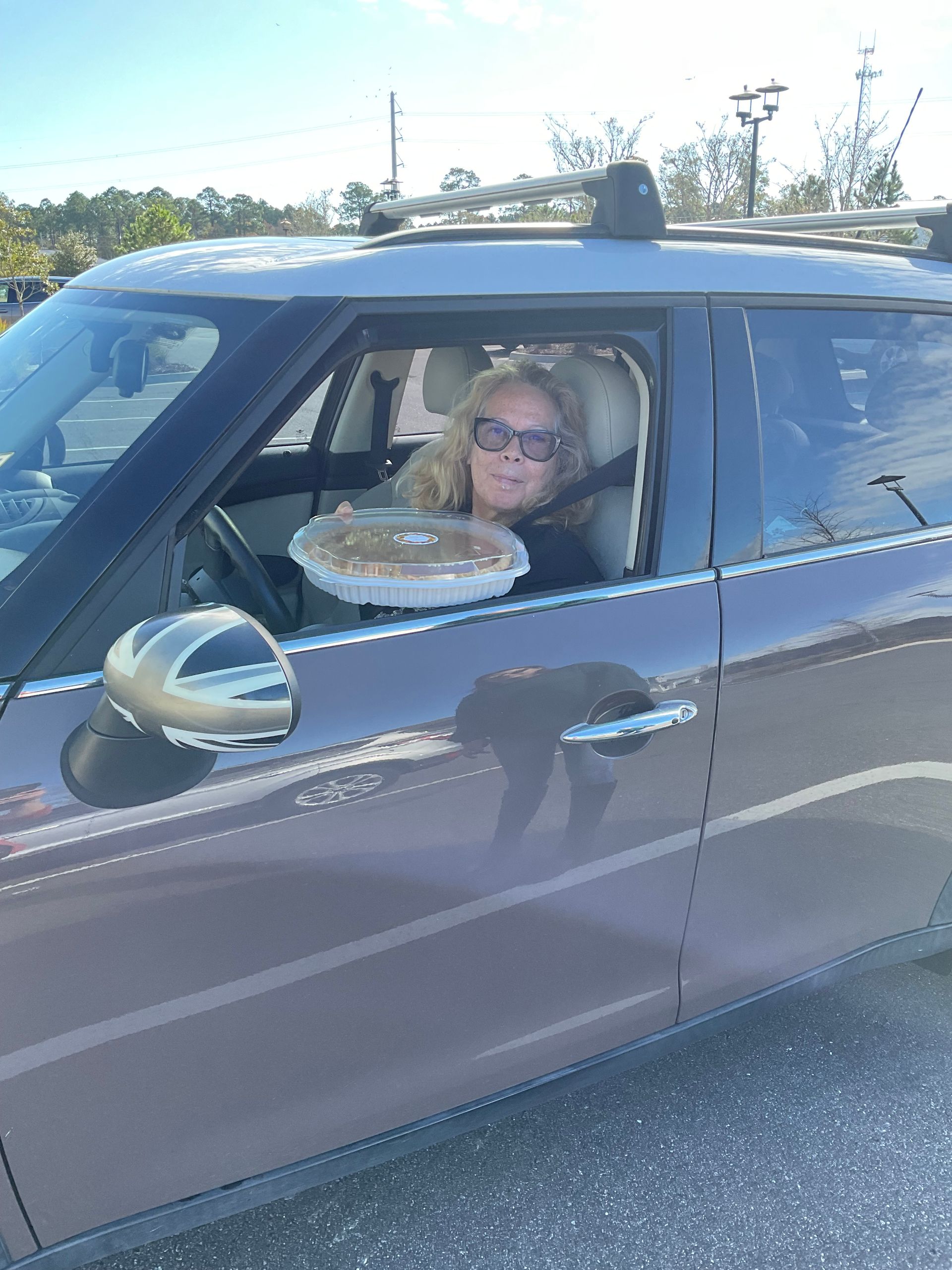 A woman is sitting in a car with a pie in her hand.