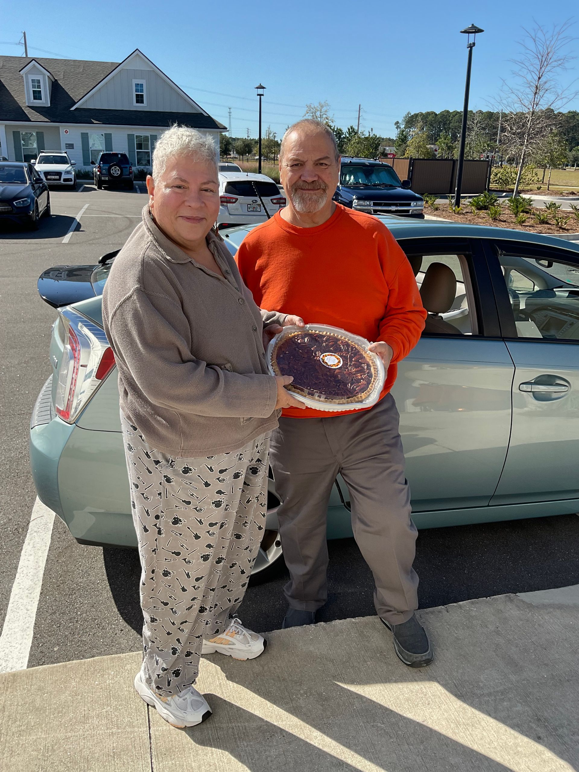 A man and a woman are standing next to a car in a parking lot.