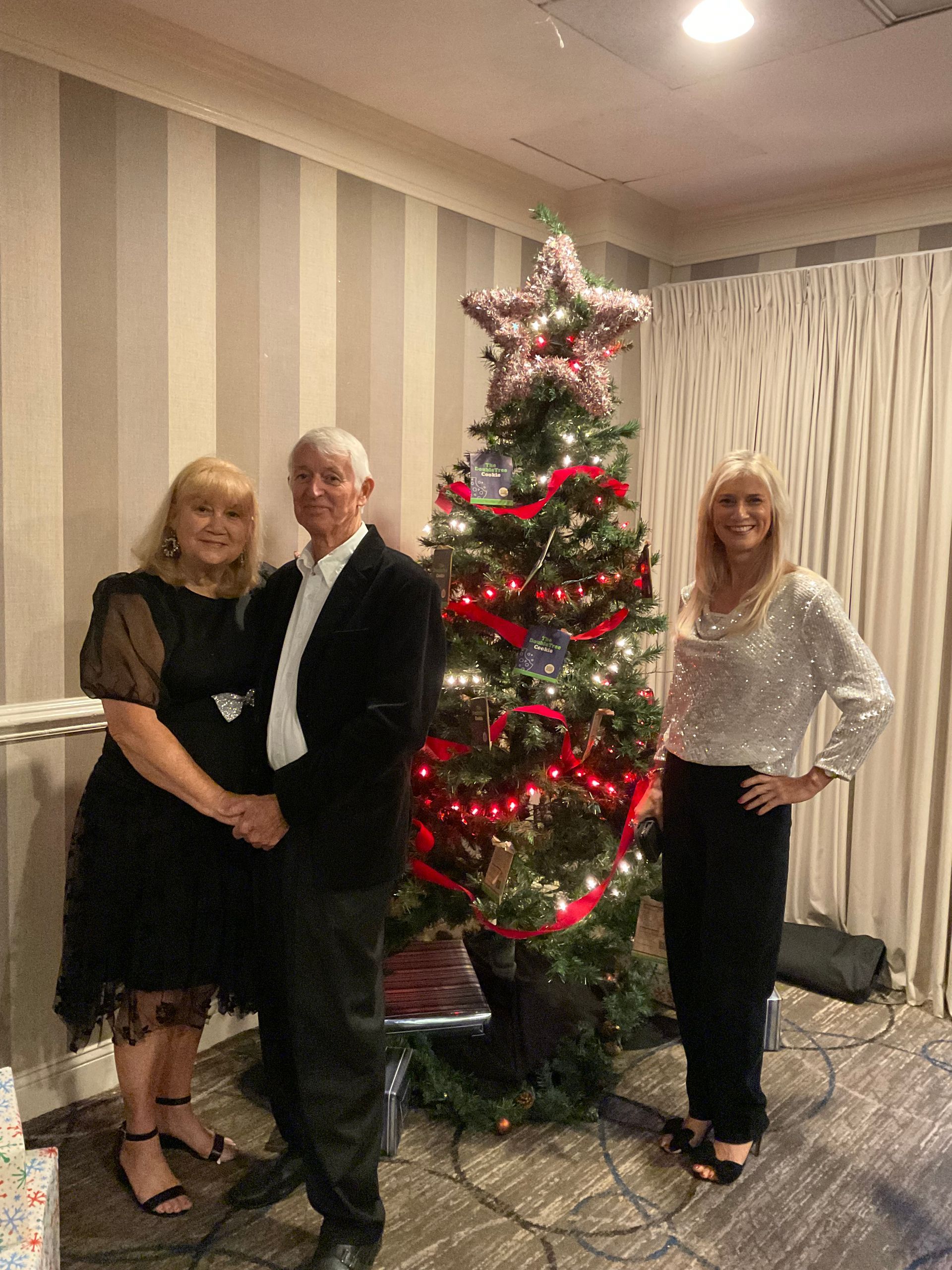 A man and two women are standing in front of a christmas tree.