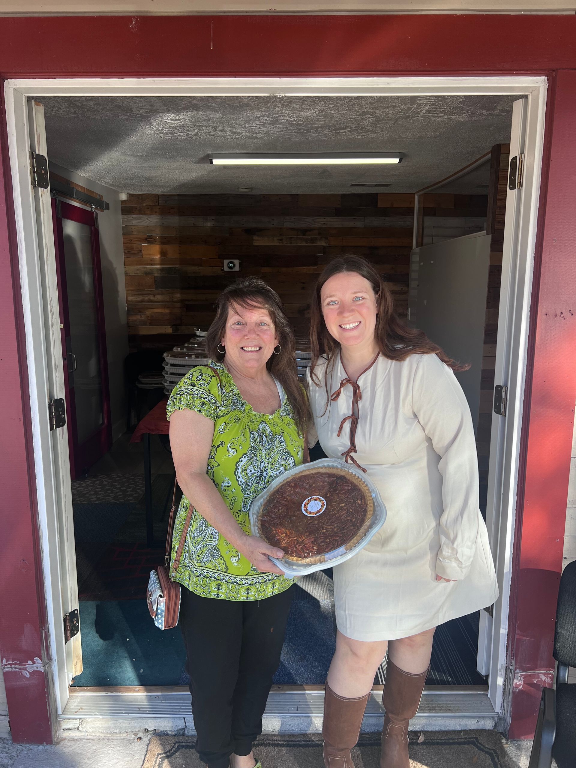 Two women are standing in a doorway holding a pie.