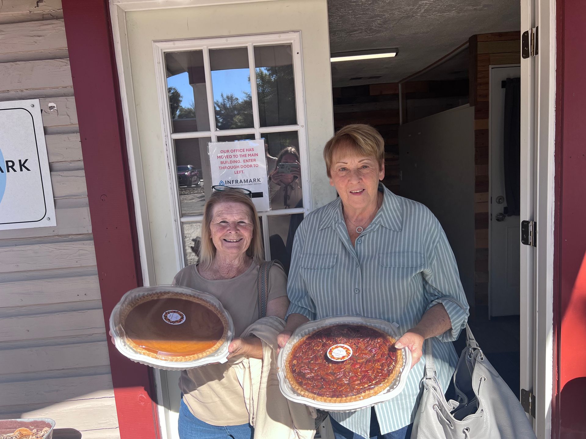 Two women are holding two pies in front of a building.