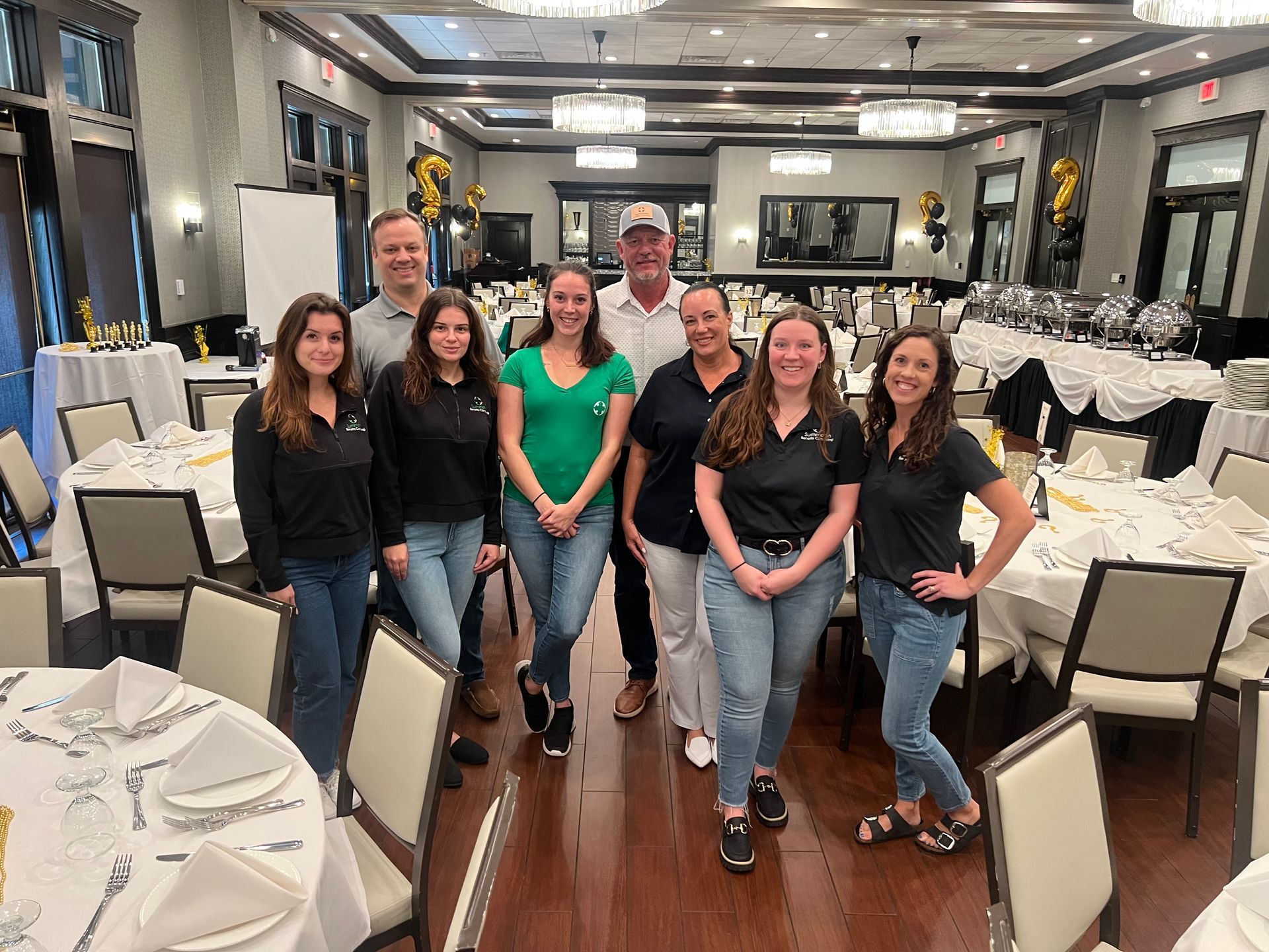 Group of people smiling in a restaurant, standing by tables set for a meal.